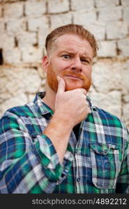 Pensive red haired hipster man with blue plaid shirt in a rural enviroment