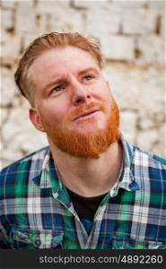 Pensive red haired hipster man with blue plaid shirt in a rural enviroment