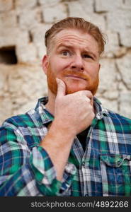 Pensive red haired hipster man with blue plaid shirt in a rural enviroment