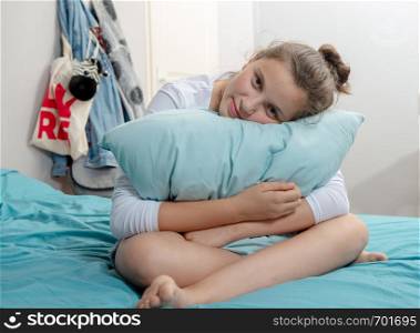 pensive teenager girl with a pillow sitting on bed