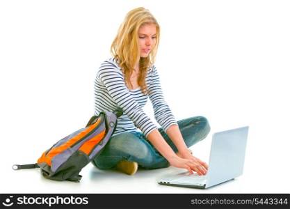 Pensive teenager sitting on floor with backpack and using laptop isolated on white &#xA;