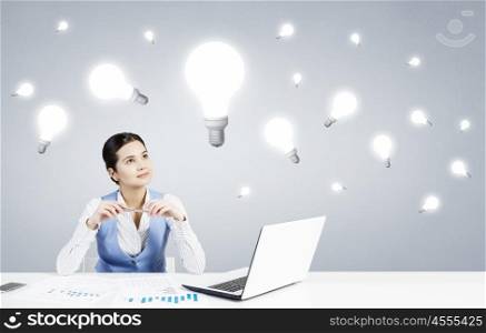 Pensive woman at work. Beautiful woman sitting at table with laptop and looking thoughtfully at light bulb