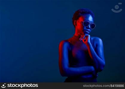 Pensive woman in sunglasses over dark studio background with copy space and neon light. Pensive woman in sunglasses over dark background