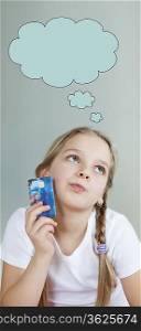 Pensive young girl holding credit card with speech bubble over gray background