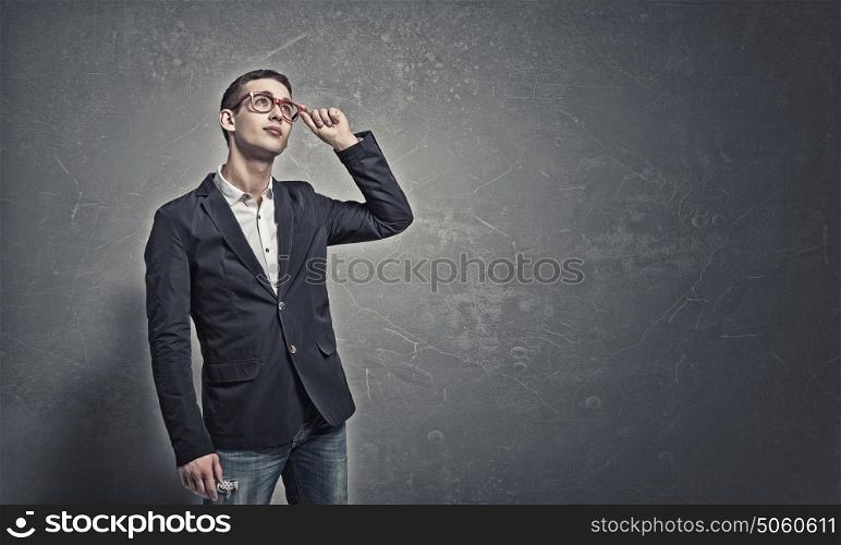 Pensive young man . Handsome young man in suit and red glasses on concrete background looking up
