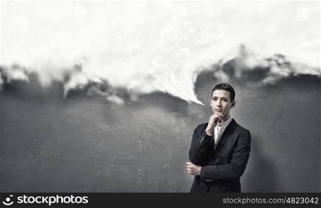 Pensive young man . Handsome young man in suit on concrete background looking in camera