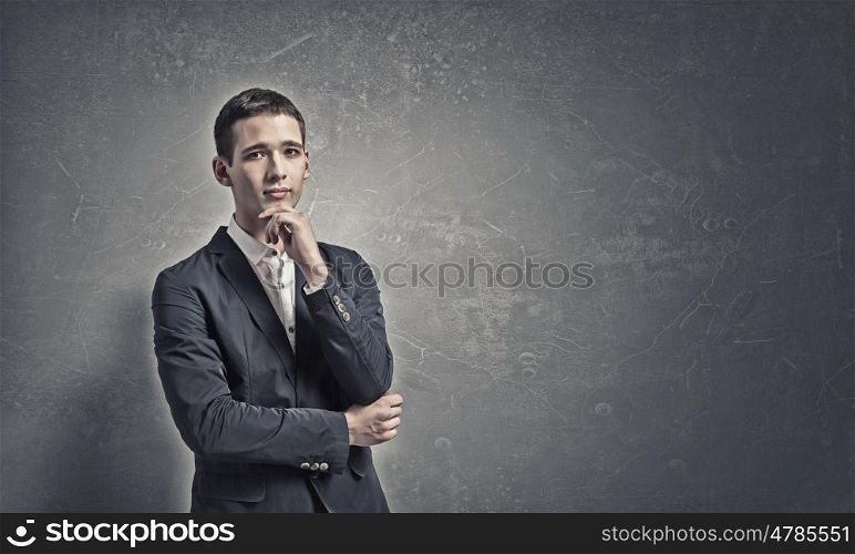 Pensive young man . Handsome young man in suit on concrete background looking up