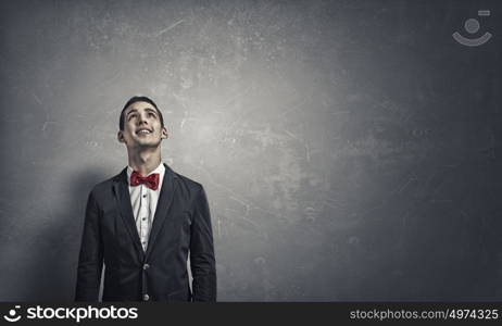 Pensive young man . Handsome young man in suit on concrete background looking up