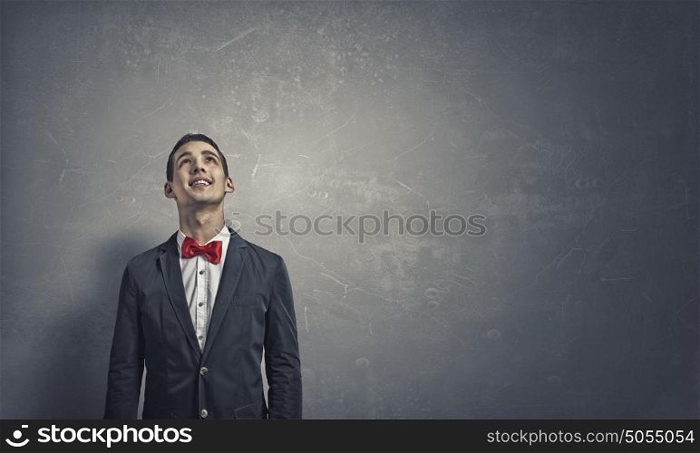 Pensive young man . Handsome young man in suit on concrete background looking up