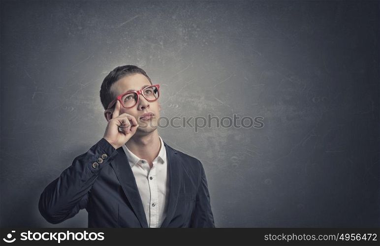 Pensive young man . Portrait of handsome young man in suit and red glasses on concrete background looking up