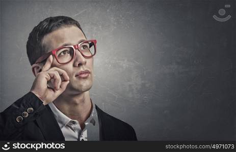 Pensive young man . Portrait of handsome young man in suit and red glasses on concrete background looking up