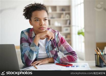Pensive young student girl sitting at table with laptop looks into distance, studying at home. Thoughtful puzzled mixed race schoolgirl ponders solution, preparing for exam, makes homework task.. Pensive mixed race student girl sitting at laptop, studying, preparing for exam, makes homework