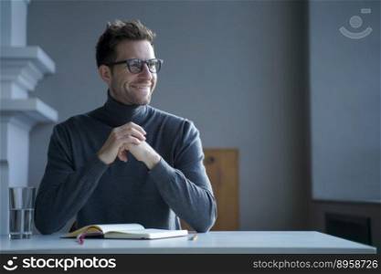 Pensively smiling male entrepreneur sitting at table in front of open agenda with folded hands and looking towards window, millennial guy german student makes important notes during work or study. Pensively smiling male entrepreneur sitting at table in front of open agenda with folded hands