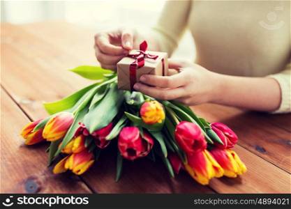 peoople, holidays and greeting concept - close up of woman holding gift box and tulip flowers