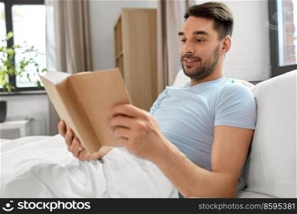 peop≤and rest concept - man reading book in bed at home. man reading book in bed at home
