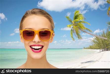 people, accessory, travel, tourism and summer vacation concept - smiling young woman in sunglasses with pink lipstick on lips over tropical beach with sea and palm tree background