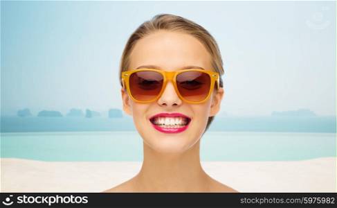people, accessory, vacation, travel and fashion concept - smiling young woman in sunglasses with pink lipstick on lips over infinity edge pool background