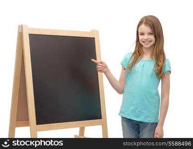 people, advertisement and education concept - happy little girl pointing finger to blackboard