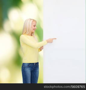 people, advertisement and sale concept - happy woman in sweater pointing finger to blank white board