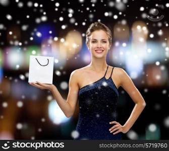 people, advertisement, christmas holidays and sale concept - smiling woman with white blank shopping bag over night lights and snow background