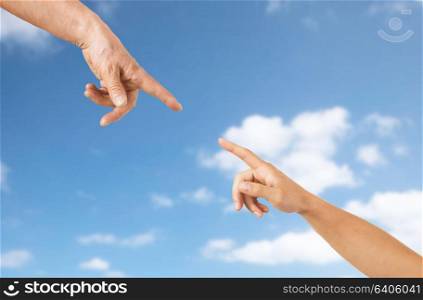 people, age and body parts concept - close up of senior and young woman hands pointing finger over blue sky and clouds background. close up of senior and young woman hands