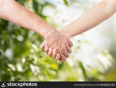people, age and charity concept - close up of senior and young woman holding hands over green natural background. close up of senior and young woman holding hands