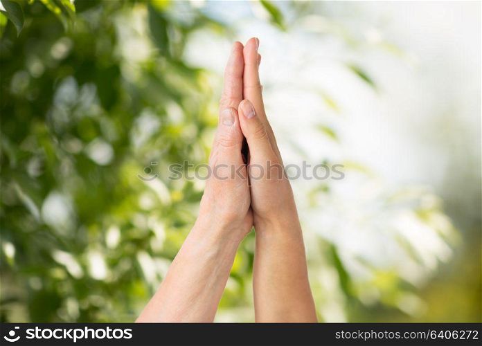 people, age and charity concept - close up of senior and young woman touching hand over green natural background. close up of senior and young woman touching hands