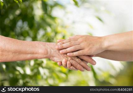 people, age and charity concept - close up of senior and young woman holding hands over green natural background. close up of senior and young woman holding hands
