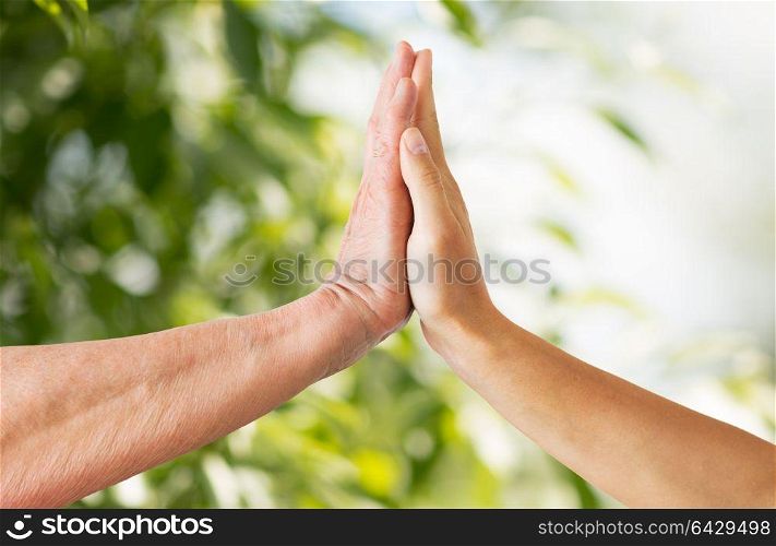 people, age and charity concept - close up of senior and young woman hands touch over green natural background. close up of senior and young woman hands touch