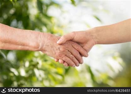 people, age, family and support concept - close up of senior woman and young woman holding hands over green natural background. close up of senior and young woman holding hands