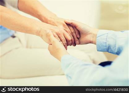 people, age, family, care and support concept - close up of senior and young woman holding hands
