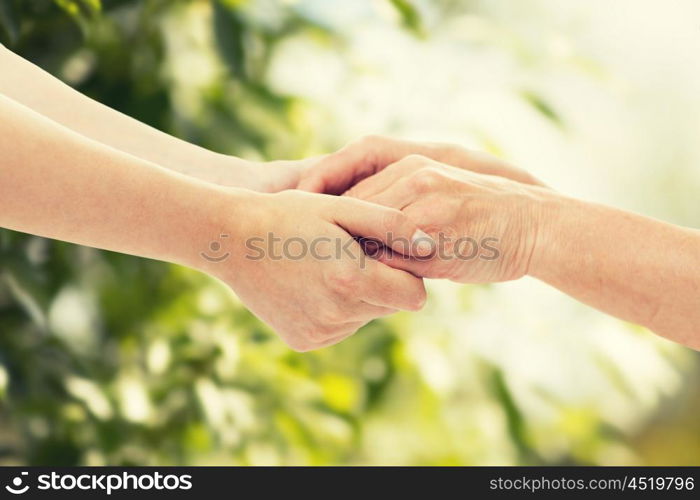 people, age, family, care and support concept - close up of senior woman and young woman holding hands over green natural background