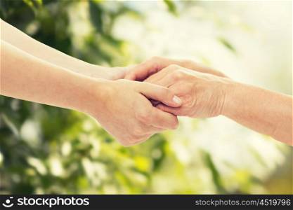 people, age, family, care and support concept - close up of senior woman and young woman holding hands over green natural background