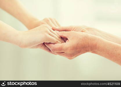 people, age, family, care and support concept - close up of senior woman and young woman holding hands