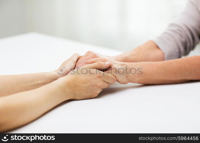 people, age, family, care and support concept - close up of senior woman and young woman holding hands