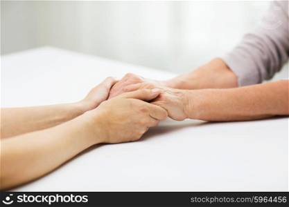 people, age, family, care and support concept - close up of senior woman and young woman holding hands