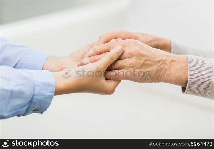 people, age, family, care and support concept - close up of senior and young woman holding hands