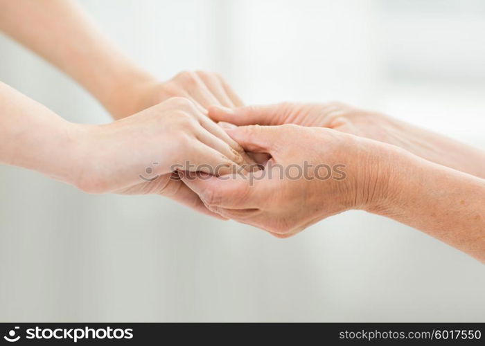 people, age, family, care and support concept - close up of senior woman and young woman holding hands