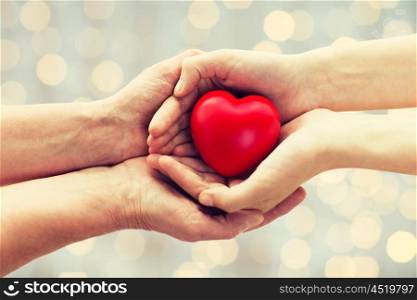 people, age, family, love and health care concept - close up of senior woman and young woman hands holding red heart over lights background