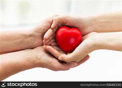 people, age, family, love and health care concept - close up of senior woman and young woman hands holding red heart
