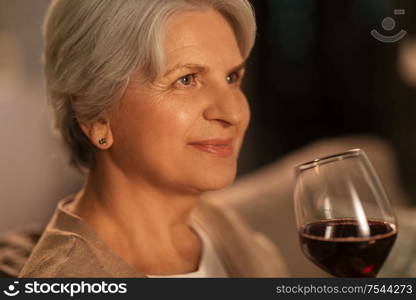 people, alcohol and drinks concept - close up of happy senior woman drinking red wine from glass at home in evening. senior woman drinking red wine at home in evening