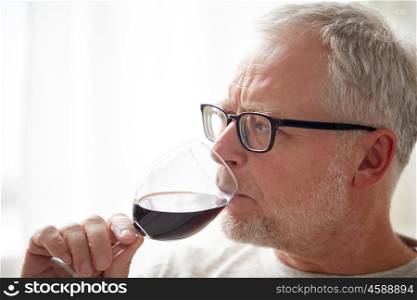 people, alcohol and drinks concept - close up of senior man drinking red wine from glass at home