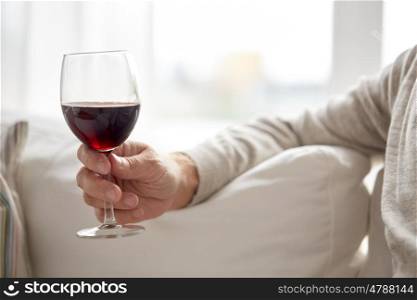 people, alcohol and drinks concept - close up of senior man hand holding glass with red wine at home