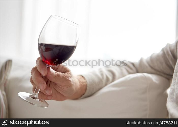 people, alcohol and drinks concept - close up of senior man hand holding glass with red wine at home