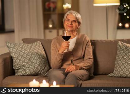 people, alcohol and drinks concept - happy senior woman drinking red wine from glass at home in evening. senior woman drinking red wine at home in evening