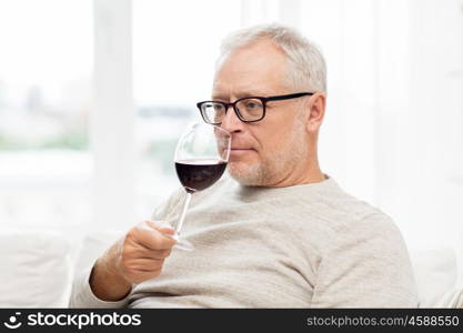 people, alcohol and drinks concept - senior man drinking red wine from glass at home