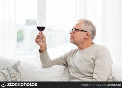 people, alcohol and drinks concept - senior man drinking red wine from glass at home