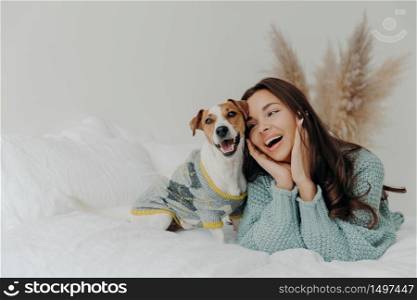 People and animals concept. Joyful pretty young woman express love to dog, spends leisure time with pet, lie together on bed, looks tenderly at animal, feels not bored with true loyal friend
