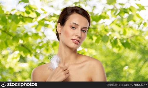 people and beauty concept - beautiful woman with feather touching her face skin over green natural background. beautiful woman with feather touching her face