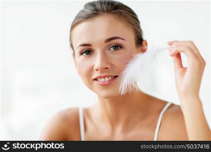 people and beauty concept - beautiful woman with feather touching her face skin at home bedroom. beautiful woman with feather touching her face